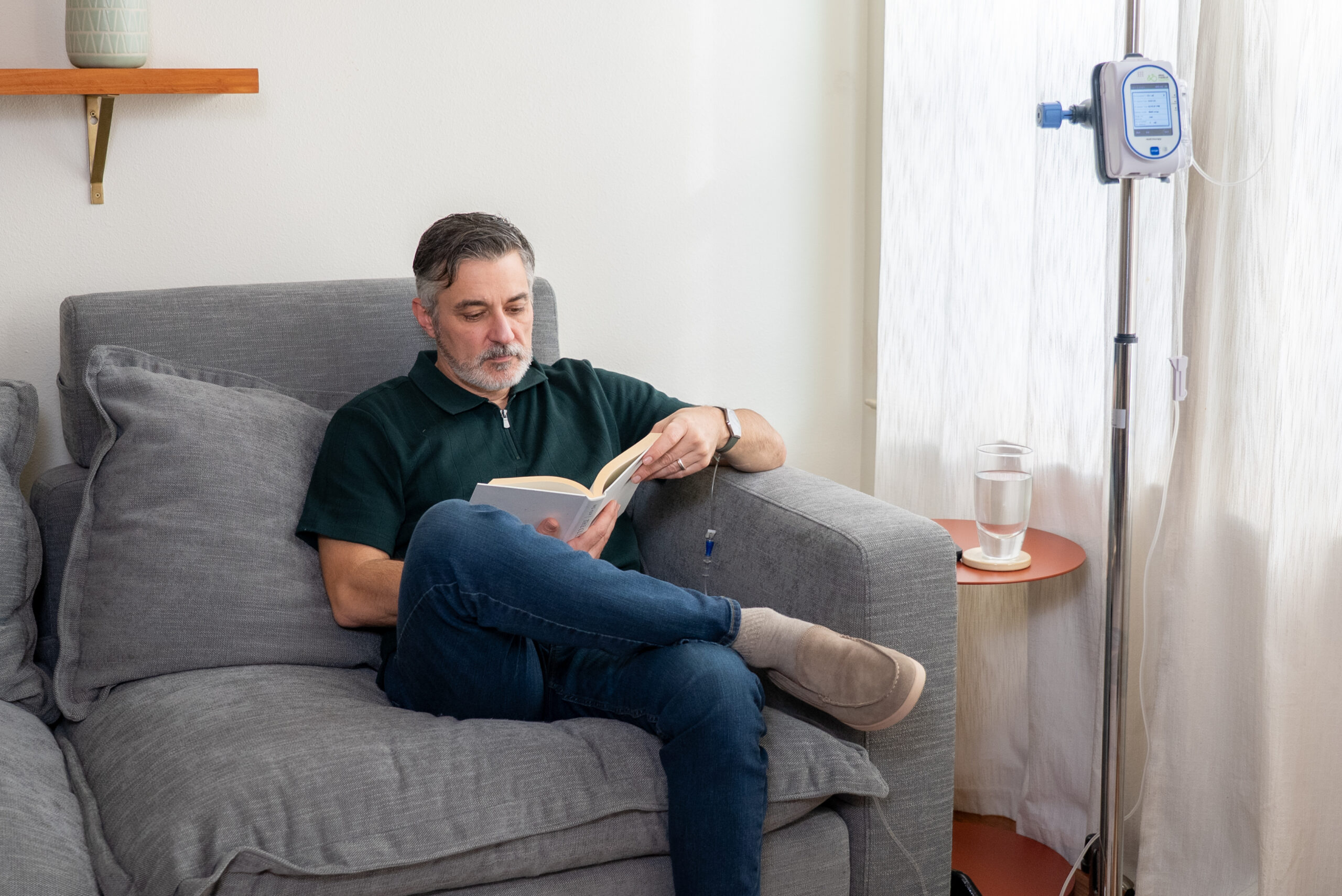 AOM Patient at home on the sofa reading a book while receiving IVIG treatment.
